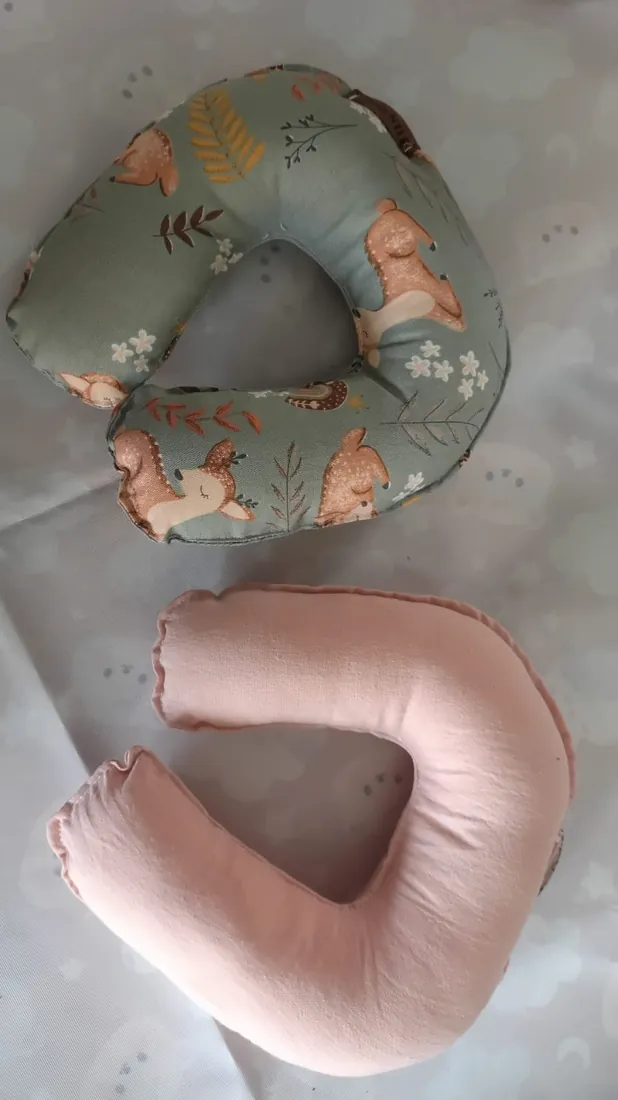 Dos almohadas cervicales en U, una verde con ciervos y otra rosa lisa
